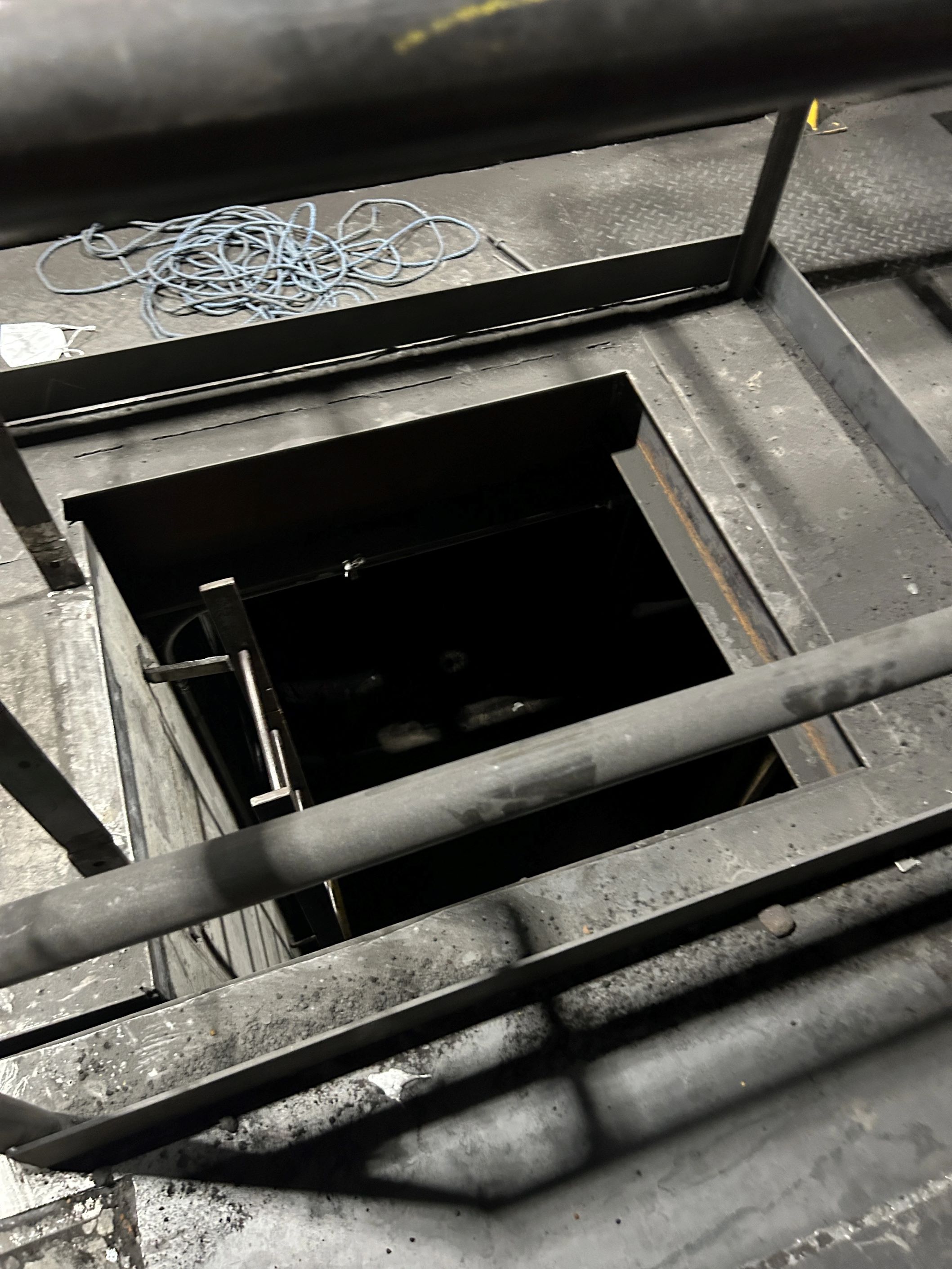 Image of a mysterious dark hole in the floor. A ladder leads down into it, but it is too dark to see in.